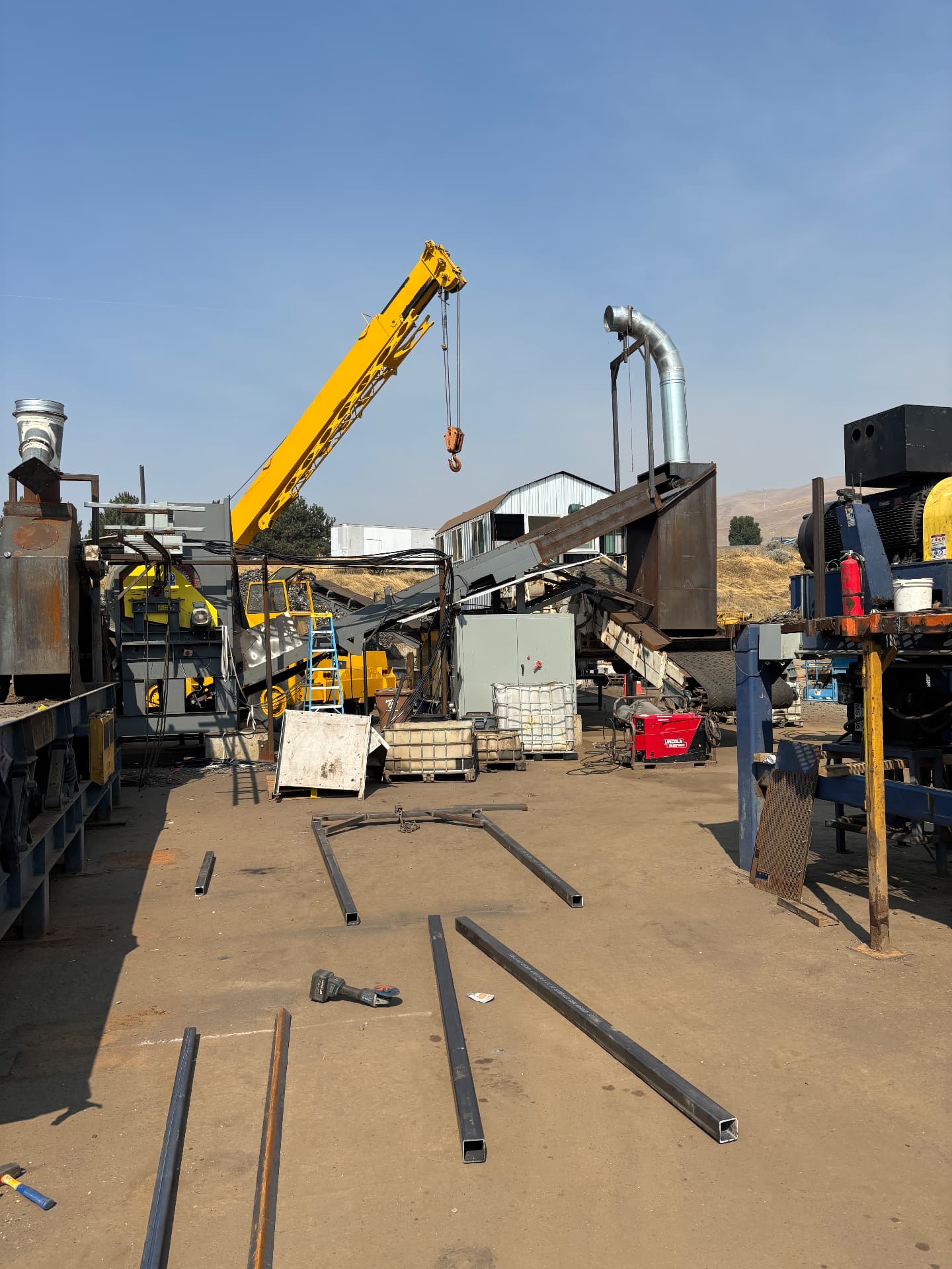 Steel tubing laid out for fabrication at an industrial equipment site with a crane and equipment in view