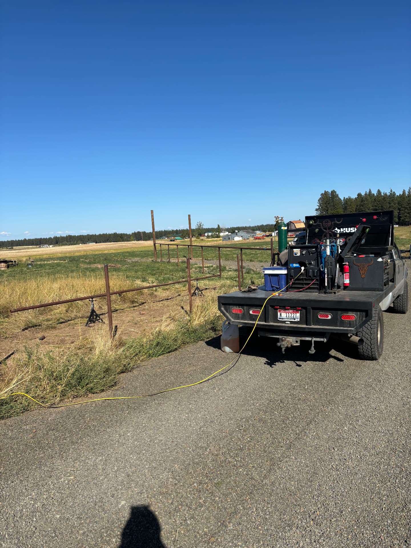 Kobar Welding mobile rig set up beside a steel pipe fence under construction on a ranch, with rails supported on jack stands
